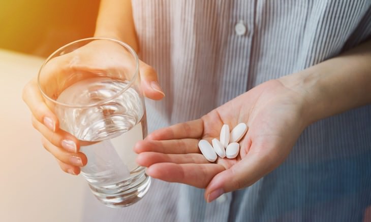 15 questions to ask doctor during exam woman holding pills in one hand and a glass of water in the other hand