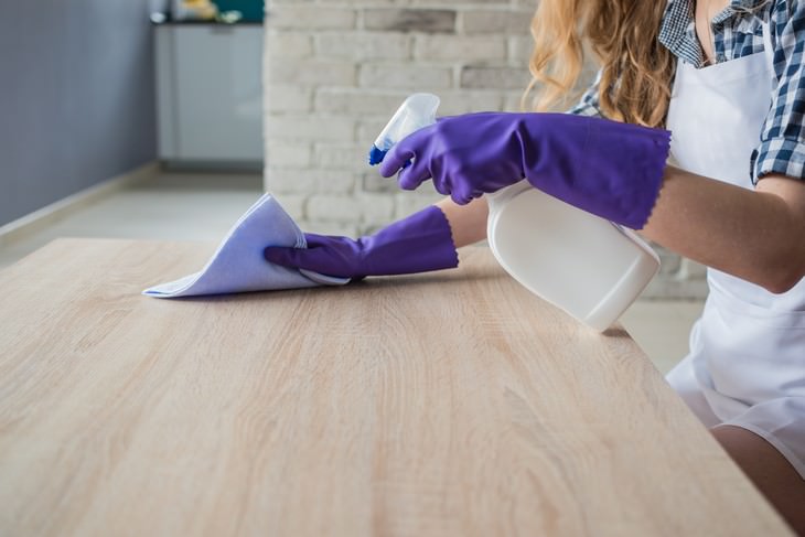 Furniture Cleaning Mistakes woman in gloves cleaning table with rag and spray