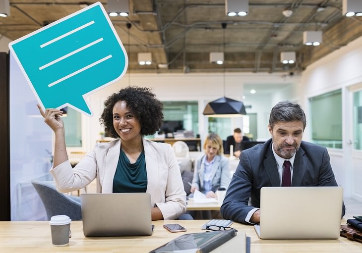 language learning woman holding a conversation sign and a man working on a laptop