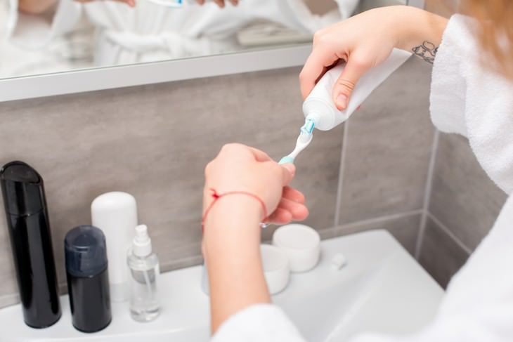 tips on how to lower aluminum exposure woman applying toothpaste to toothbrush in bathroom