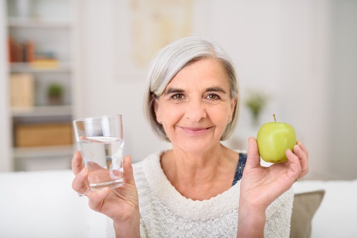 dehydration in seniors elderly woman holding a glass of water in one hand and an apple in the other hand