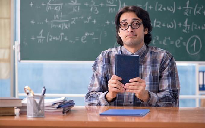 Math quiz: math teacher in front of blackboard with equations holding book
