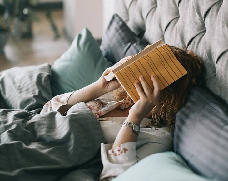 irrelevant slang woman laying in bed covering her head with a book