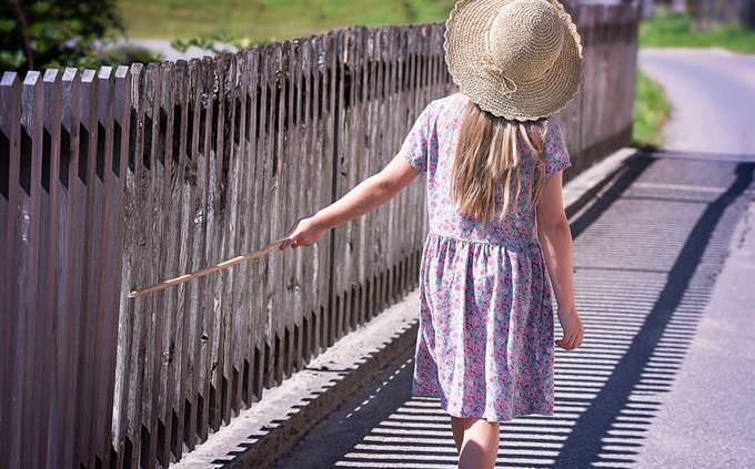 בחם את עצמך: ילדה מטיילת לצד גדר עם מקל בידה