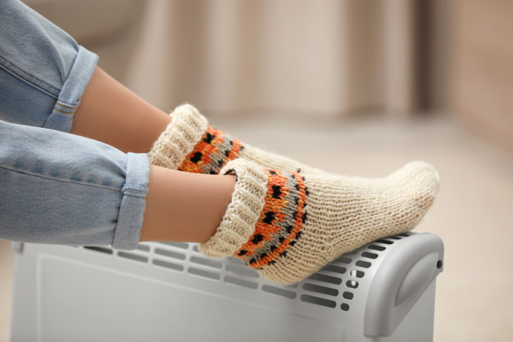 Cold Feet Causes and Remedies woman wearing warm socks and warming up feet near the radiator