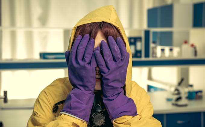 girl in chemistry lab with gloved hands covering her face