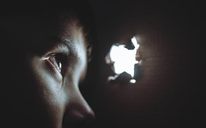 man looking out cardboard hole