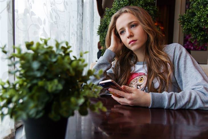 young woman with a phone sitting at the table sad