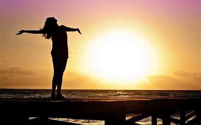 A silhouette of a woman raising her hands up in front of a sunset