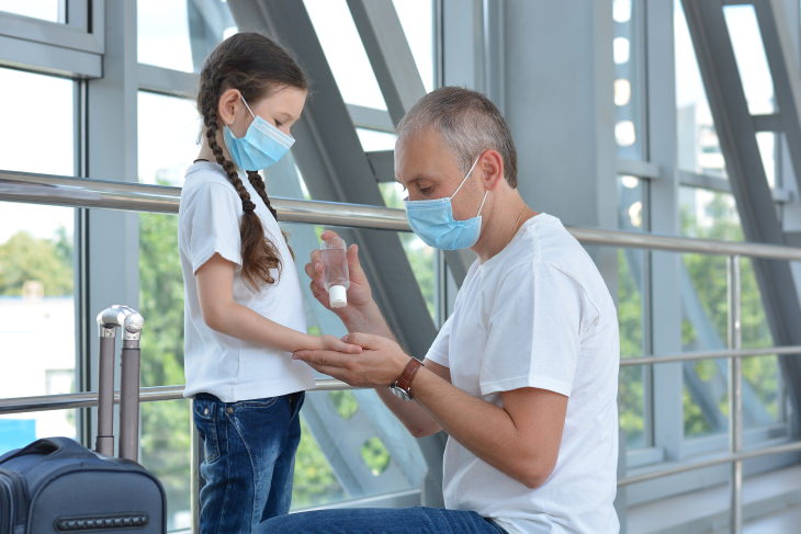 COVID-19: How to Fly Safely During a Pandemic man helping girl disinfect her hands with hand sanitizer