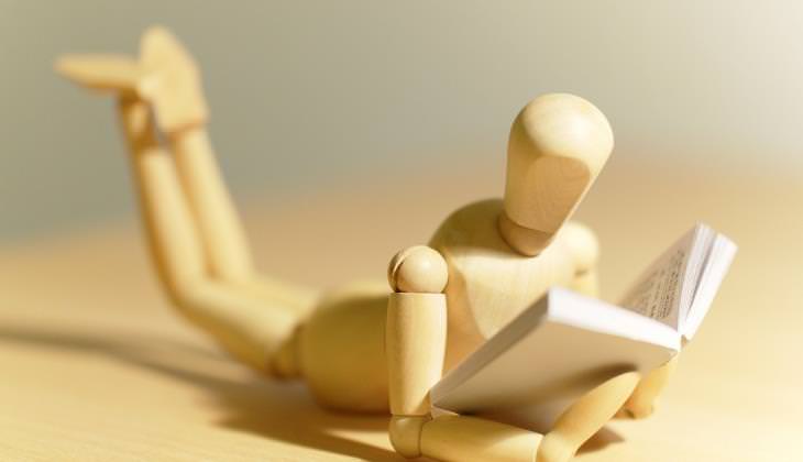 wooden man lying on stomach reading a book