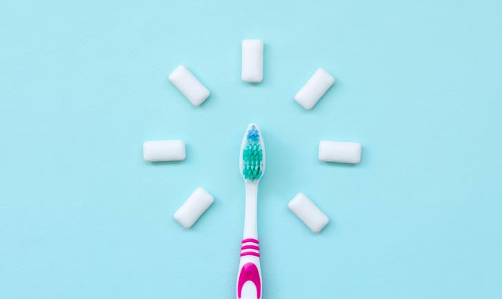 photo of pink toothbrush surrounded by chewing gum, blue background 