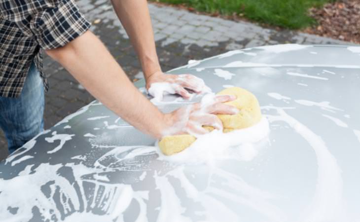 man cleaning car hood with a sponge