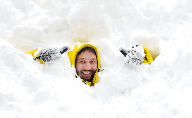 Build cold tolerance - man with yellow coat smiling buried in snow