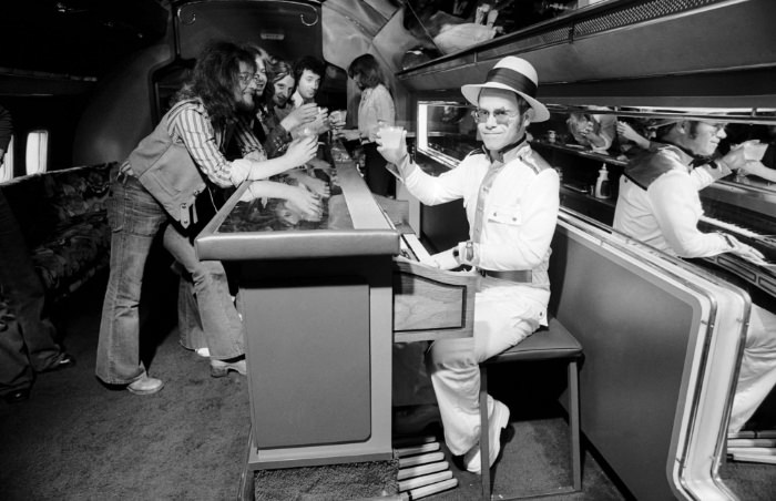 Elton with Elton hosting a party in his private jet, 1974