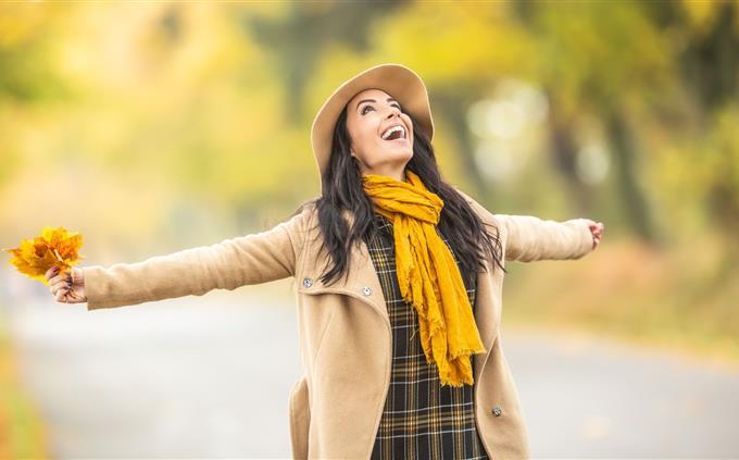 Find the differences in autumn: A woman in autumnal clothing raises her arms to her sides