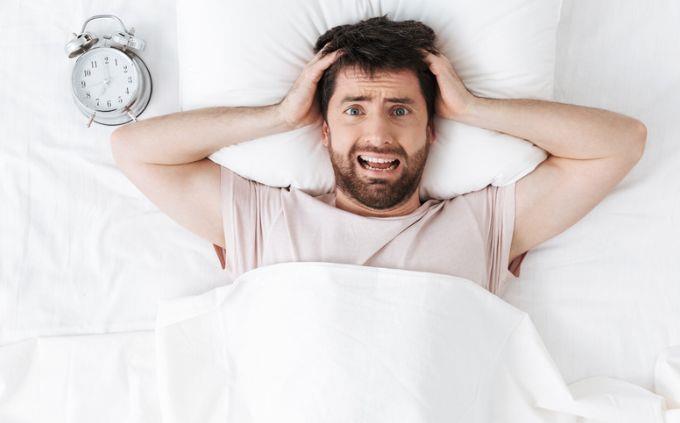 Are you a liar: a stressed man next to an alarm clock in bed