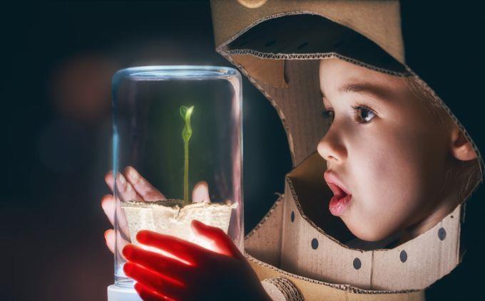 Which planet matches your personality: A boy in an astronaut costume looks at a plant sealed in glass