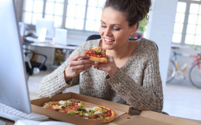 Are you worn out or stressed: Woman eating pizza in the office
