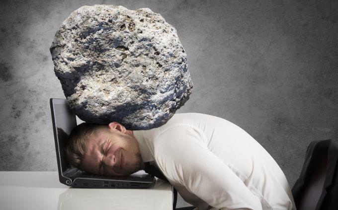Are you worn out or stressed: Man with a stone pressing on his head directly on a laptop