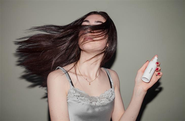 מרכיב מזיק לשיער בשמפו: אישה מנפנפת בשיערה ומחזיקה תכשיר לשיער בידה