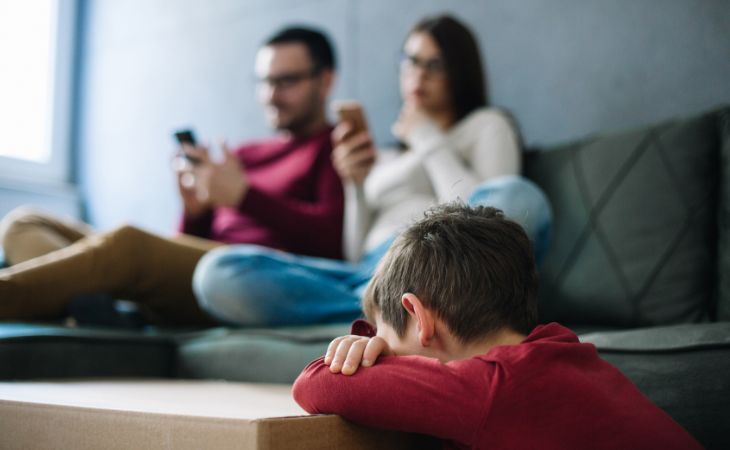 How to recognize toxic family dynamics: Parents on the phone while a child rests his head on the table between his hands