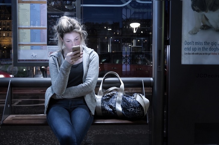 Surprising brain facts: Woman at a bus stop late at night looking at a smartphone