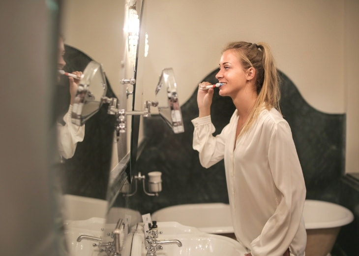 Actions and habits that cause lower back pain: Woman brushing teeth in front of the mirror