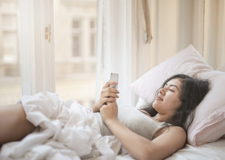 Actions and habits that cause lower back pain: Woman using her smartphone while lying in bed