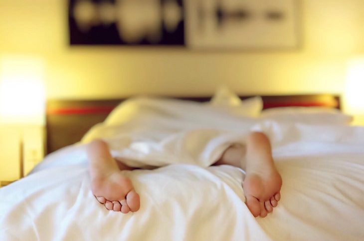 Methods to overcome insomnia: A person lying in bed with both feet sticking out from under the blanket