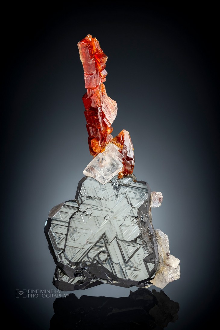 Red Uvite cluster perched on translucent rhombohedral Magnesite on lustrous Haematite crystal.