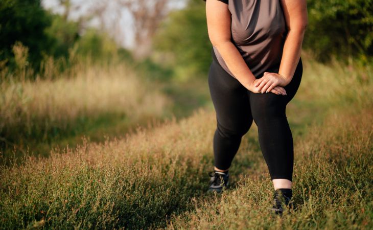 באיזו שעה כדאי להתאמן למניעת סיכונים בריאותיים בעודף משקל: אישה כבדת משקל מבצעת מתיחות בטבע