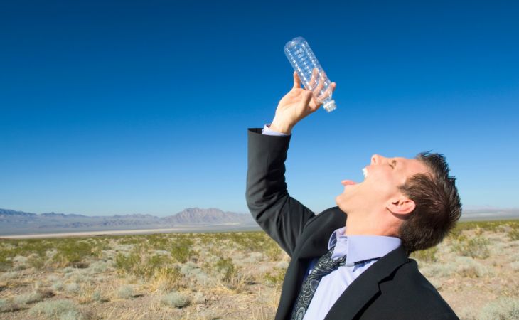 man drinking last drop from a bottle in the desert