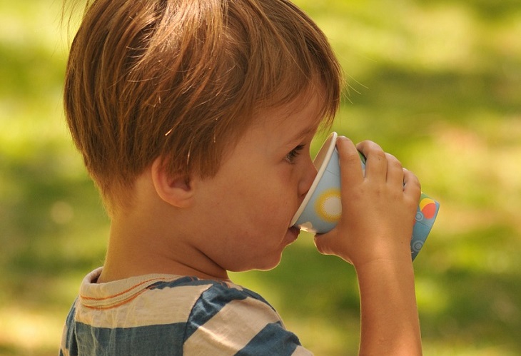 Tips to prevent bedwetting: Child drinking from a cup with the morning sun in the background