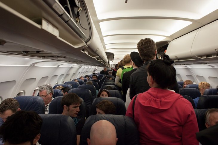 Things to avoid on a flight: passengers standing in the aisle of an airplane next to seated passengers