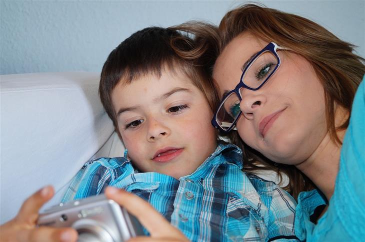 Parenting Styles: Mother lying next to her son and they are looking at pictures on a camera together