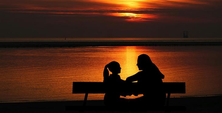 Parenting Styles: Mother and daughter sitting on a bench talking by the sea at sunset