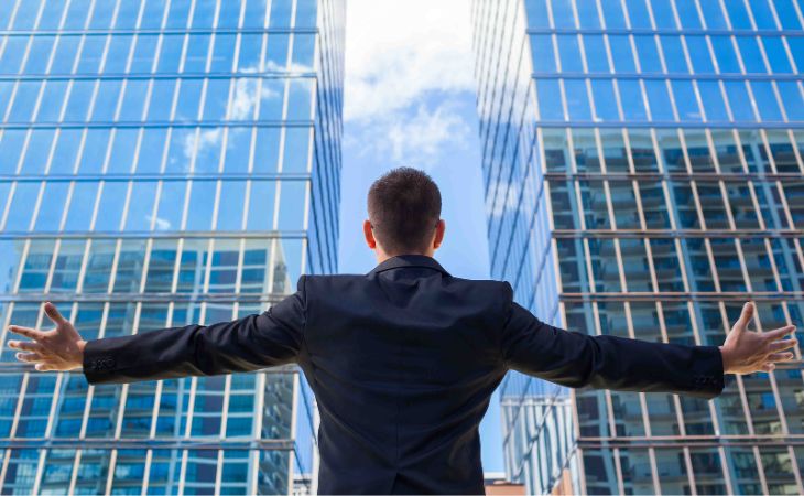 Shiny object syndrome: Man in suit raising arms towards skyscrapers