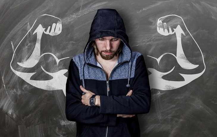 Phrases to get life back on track: Person standing with crossed arms facing a board with a drawing of muscular arms on it