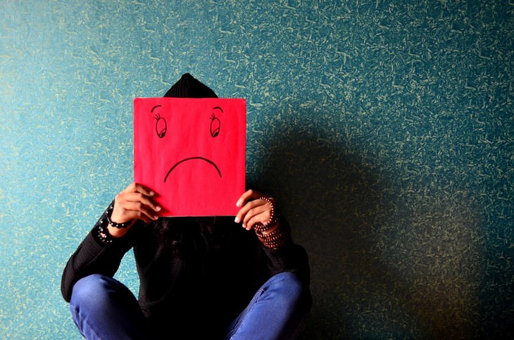 Phrases to get life back on track: Man sitting holding paper with a drawing of a sad face on it