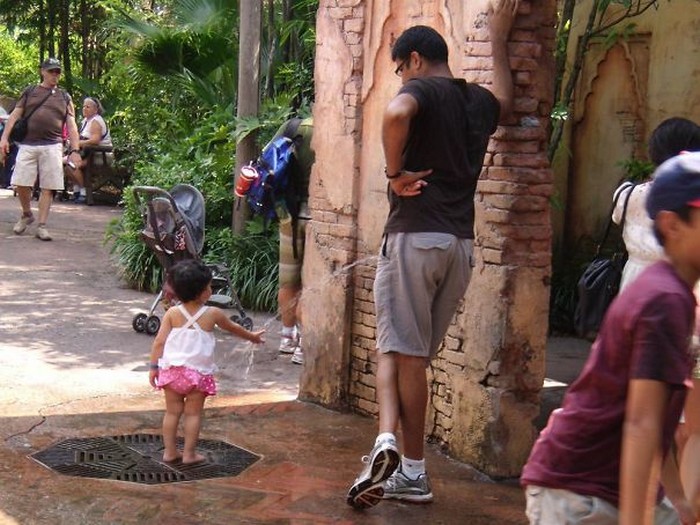 Funny perfectly timed photos: man standing near small girl playing in fountain