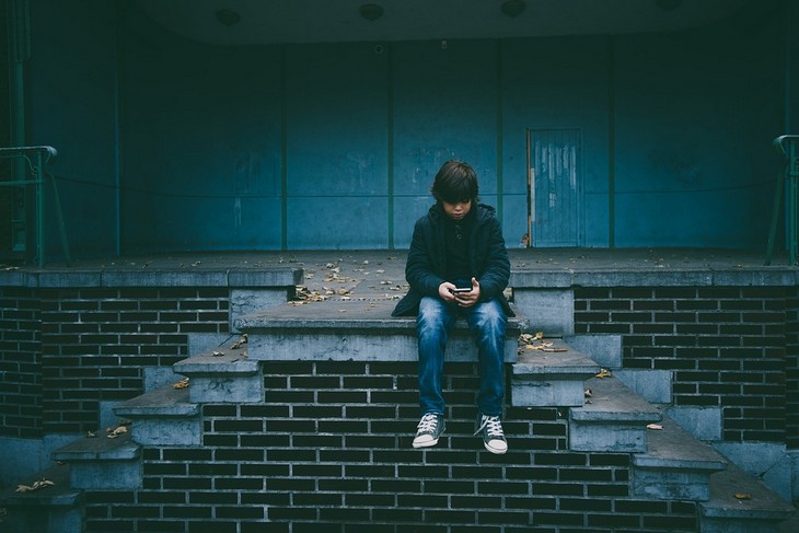 Problems caused by smartphone use in children: child sitting on a staircase holding a phone