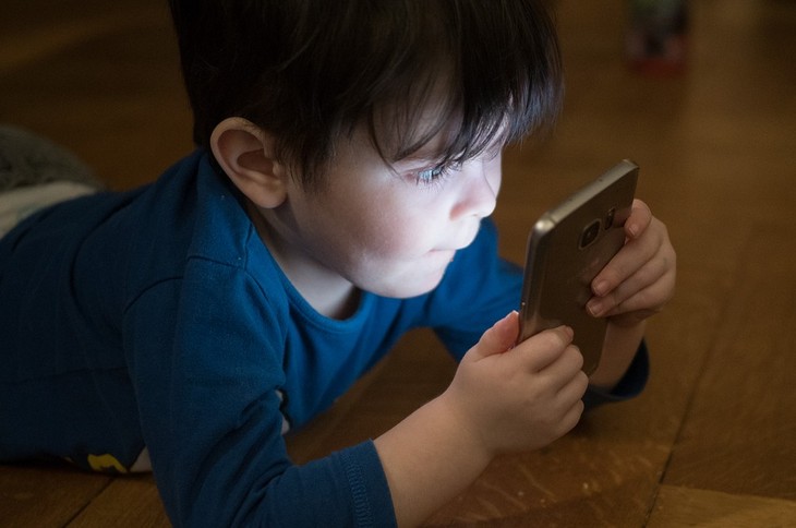 Problems caused by smartphone use in children: a small child lying on the floor holding a mobile phone