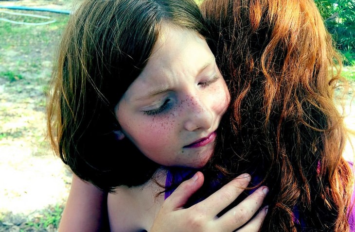 A red-haired child hugging her mother with closed eyes