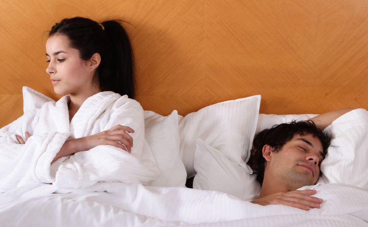 What to do if you feel lonely in marriage: Man sleeping and woman sitting on the same bed with arms crossed