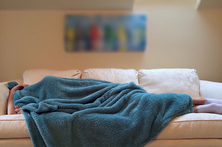 Effects of stomach problems on the body: A person lying on the couch, covering their entire body with a blanket