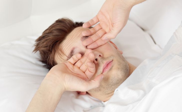 Dawn phenomenon: man rubbing eyes in bed in the morning