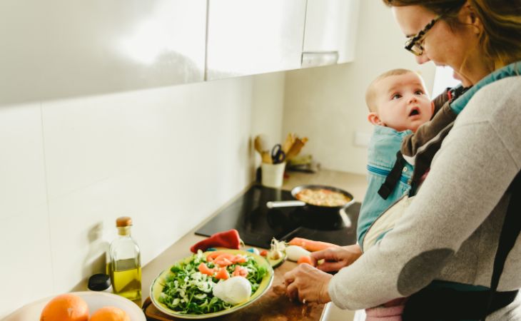 Koala Parenting: Mother cutting a salad with baby in a carrier