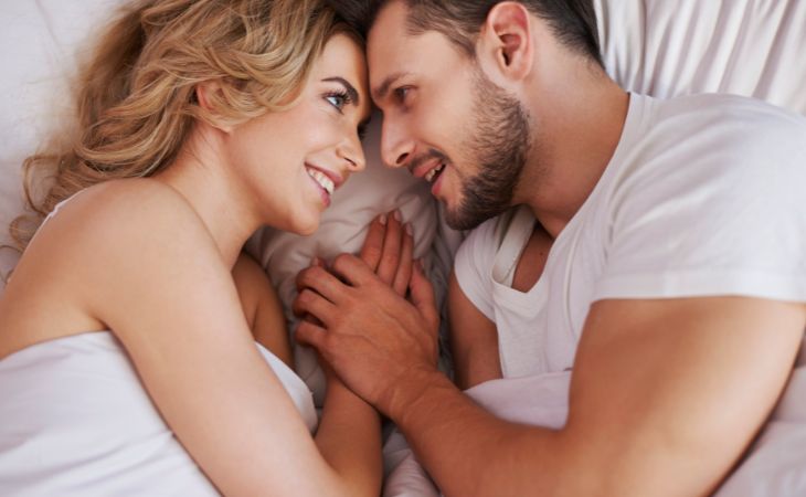 Signs that an emotionally unavailable person loves you: A couple lying in bed together, looking into each other’s eyes