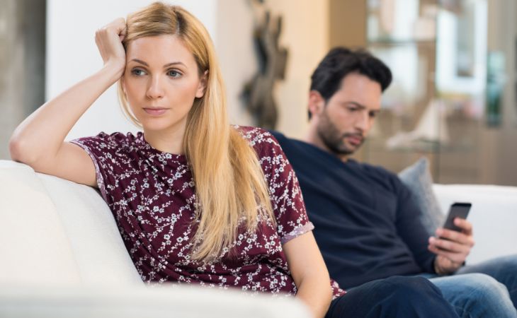 Signs that an emotionally unavailable person loves you: A frustrated woman and a man using his phone beside her